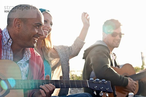 Drei erwachsene Freunde spielen Akustikgitarren am Bournemouth Beach  Dorset  UK