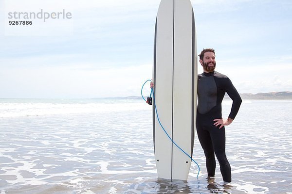 Portrait eines jungen Surfer im Meer stehend mit Surfbrett