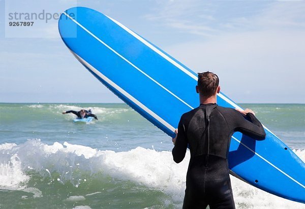 Rückansicht des männlichen Surfers mit Surfbrettbeobachtung Freund Surfen