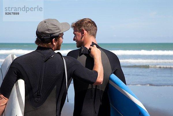 Rückansicht des männlichen Surfers beim Überprüfen des Neoprenanzug-Reißverschlusses seiner Freunde