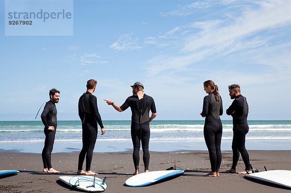 Gruppe von männlichen und weiblichen Surferfreunden beim Plaudern am Strand