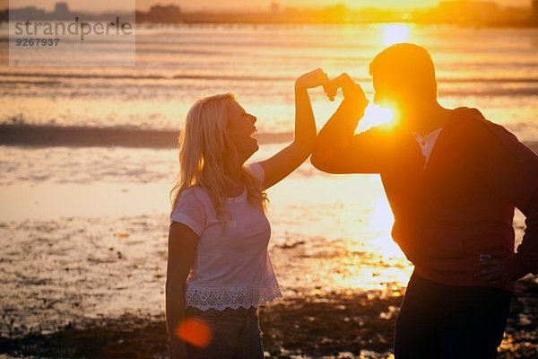 Paar bildende Herzform mit Armen am Strand bei Sonnenuntergang