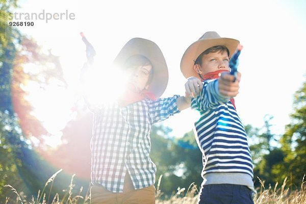 Zwei kleine Jungen als Cowboys verkleidet  die Spielzeugpistolen halten.