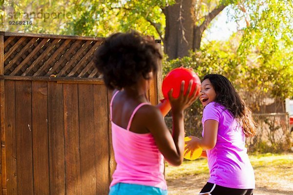 Mädchen jagen Freundin mit Wasserballon im Garten