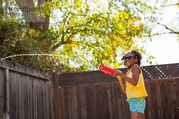 Mädchen spritzt Wasser aus Wasserpistole im Garten