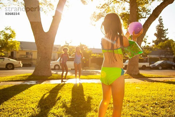 Mädchen jagen Freunde mit Wasserballon im Garten