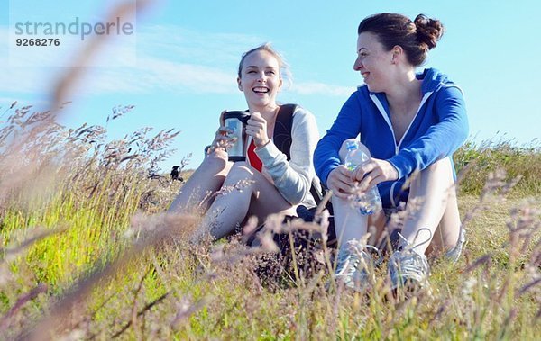 Zwei junge Frauen sitzen auf Gras  trinken und reden