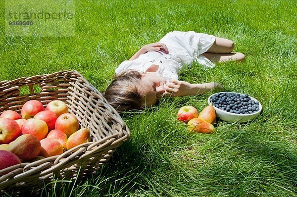 Mädchen schläft auf Gras mit Apfel- und Birnenkorb