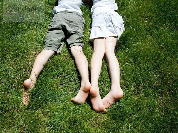 Blick über den Kopf auf die Beine der Geschwister  während sie auf Gras liegen