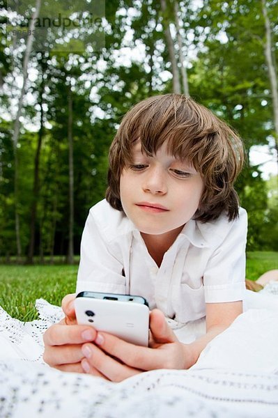 Junge liegt auf der Vorderseite und liest Nachrichten auf dem Smartphone.