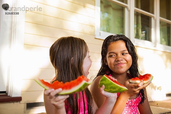 Zwei lächelnde Mädchen sitzen auf der Hausveranda mit Wassermelonenscheiben