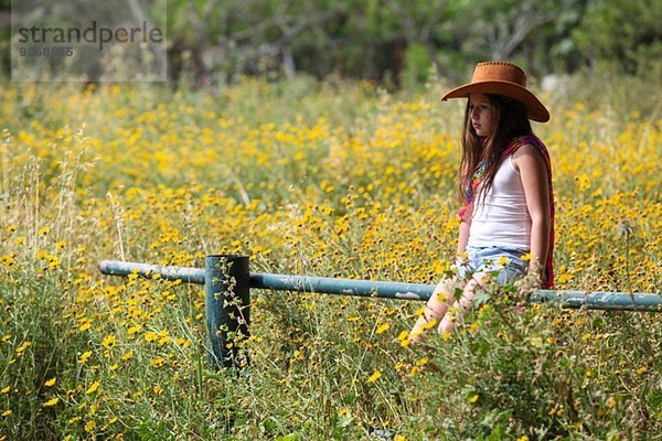 Mürrisches Mädchen mit Cowboyhut auf Zaun im Feld sitzend