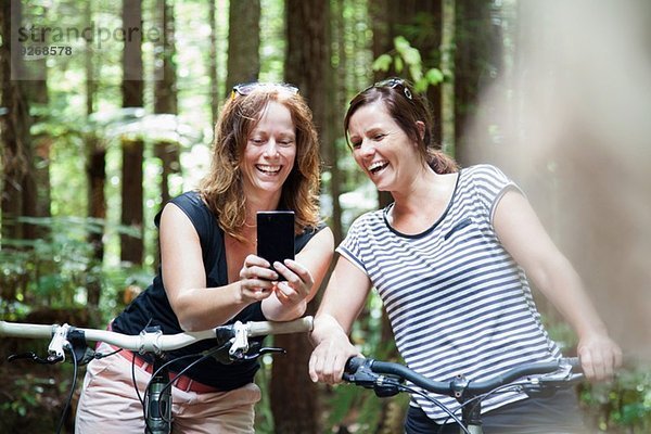 Zwei Mountainbikerinnen beim Blick auf das Smartphone im Wald