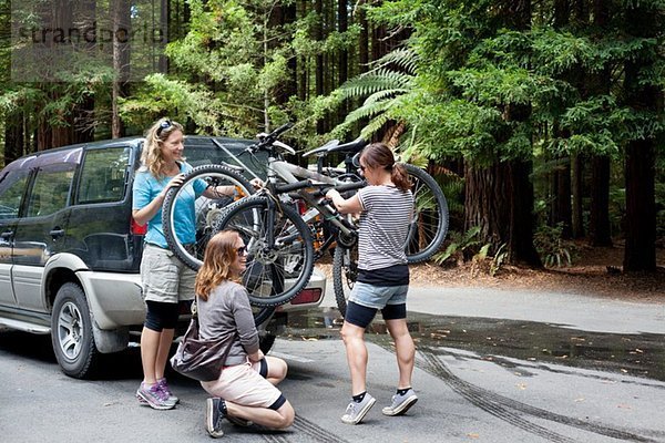 Drei Mountainbikerinnen heben Fahrräder vom Geländewagen in den Wald