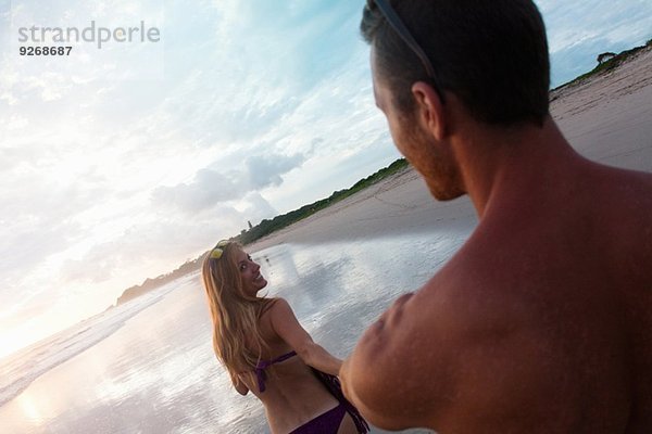 Über Schulteransicht einer erwachsenen Frau  die ihren Freund von Hand am Strand  Nosara  Guanacaste  Costa Rica führt.