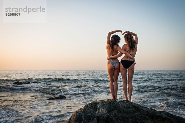 Zwei junge Frauen auf Felsen im Meer  Rückansicht