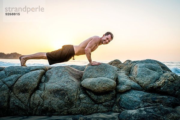 Mittlerer erwachsener Mann beim Liegestütz auf Felsen am Strand