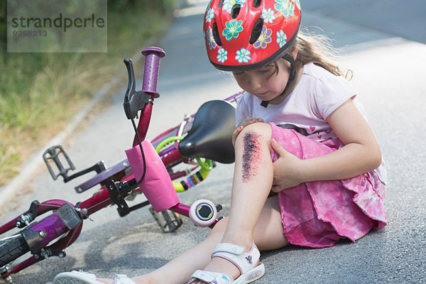 Junges Mädchen mit verletztem Bein auf der Straße sitzend mit Fahrrad