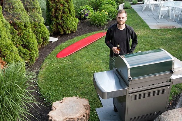 Porträt eines erwachsenen Mannes am Grill mit Bierflasche im Garten