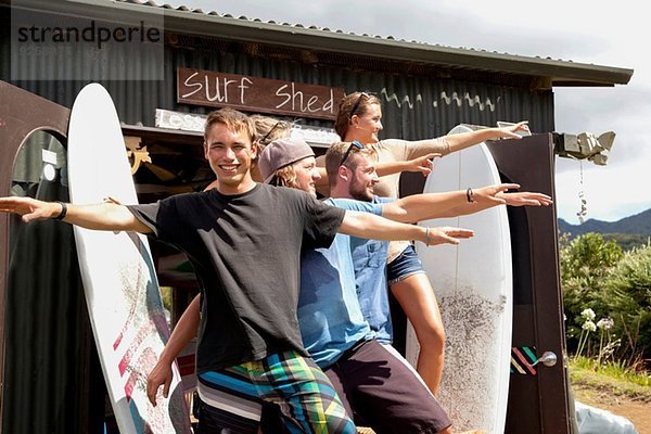 Gruppenporträt von fünf jungen erwachsenen Surferfreunden  die mit ausgestreckten Armen posieren