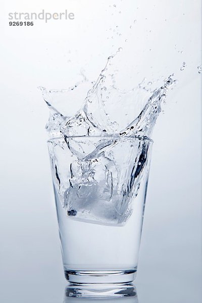 Eiswürfel  der in ein Glas mit klarem Wasser spritzt.