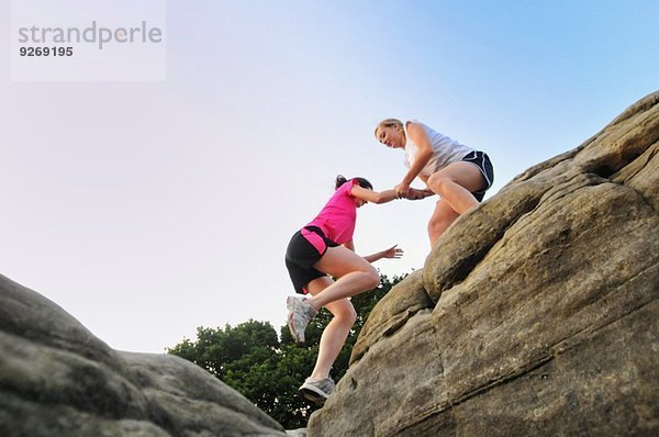Zwei junge Läuferinnen helfen sich gegenseitig auf dem Felsen.