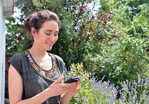Junge Frau im Garten liest Textnachricht auf dem Smartphone