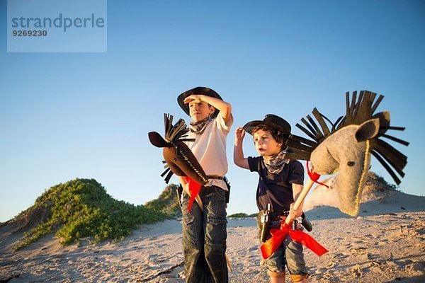 Zwei Brüder als Cowboys verkleidet  die Augen mit Händen schattieren.