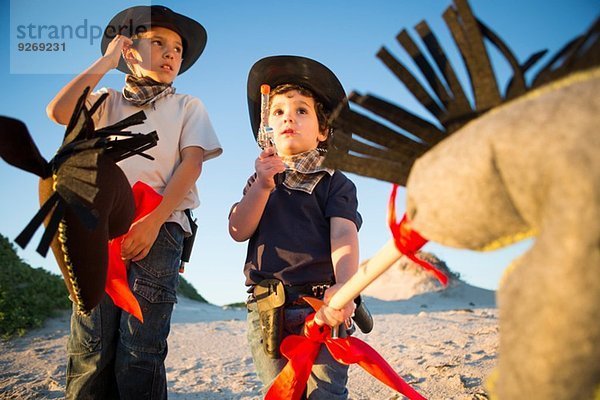 Zwei Brüder verkleidet als Cowboys mit Spielzeugpistole und Hobbypferd.