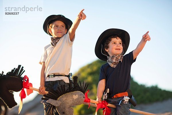 Zwei als Cowboys gekleidete Brüder  die von Sanddünen aus zeigen