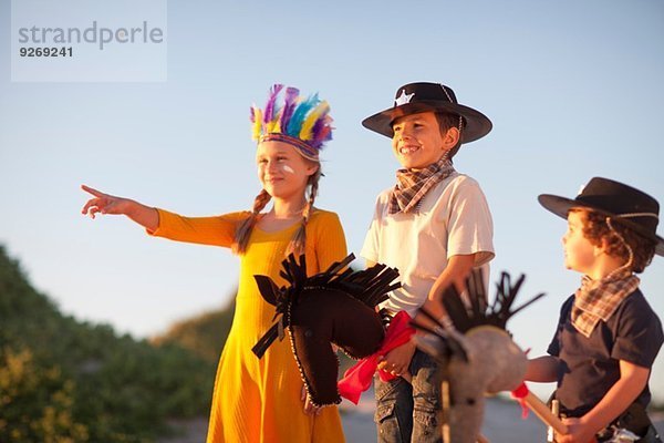 Drei Kinder  gekleidet als Indianer und Cowboys  die auf Sanddünen zeigen.