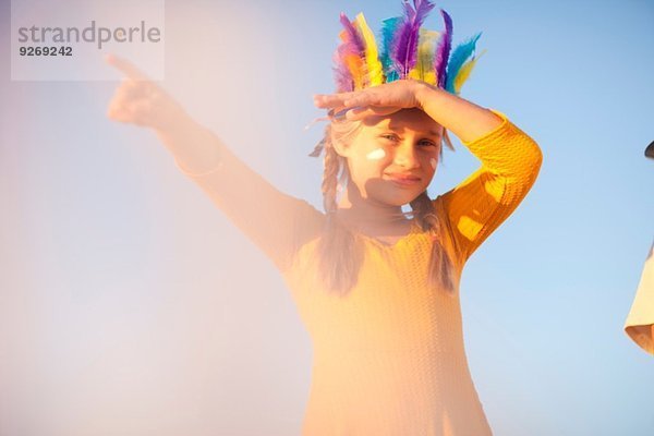 Mädchen gekleidet als Indianerin in Federkopfschmuck mit Handschattenaugen und Zeigefinger