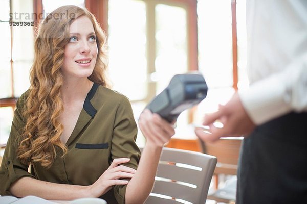 Junge Frau übergibt Kartenleser an Kellner im Restaurant