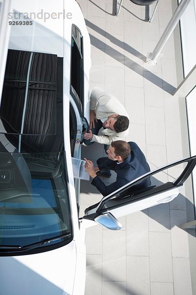 Overhead-Ansicht des Verkäufers und Kunden bei der Neuwageninspektion im Autohaus