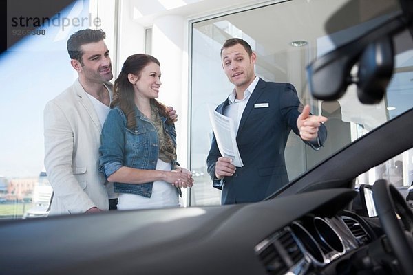 Mittleres erwachsenes Pärchen und Verkäufer im Autohaus