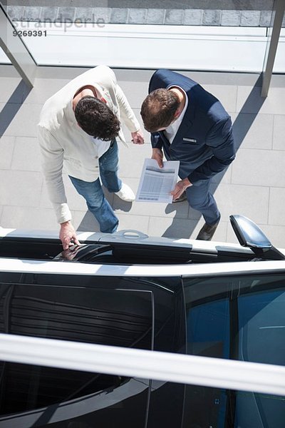 Overhead-Ansicht des Verkäufers und Kunden bei der Suche nach Neuwagen im Autohaus