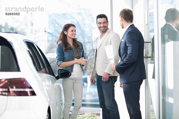 Verkäufer und mittleres erwachsenes Paar beim Plaudern im Autohaus