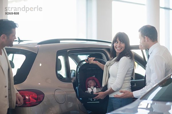 Mittleres erwachsenes Paar mit Baby Girl beim Ausprobieren des Kindersitzes im Autohaus