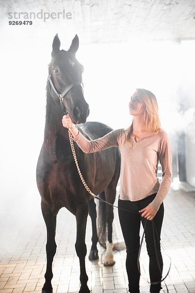 Junge Frau im Stall stehend mit schwarzem Pferd