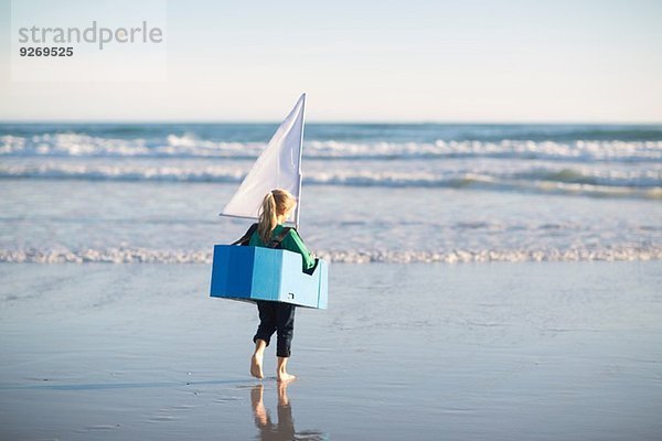 Mädchen rennt mit Spielzeugboot ins Meer