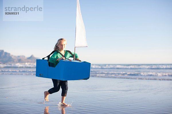 Mädchen läuft mit Spielzeugboot am Strand entlang