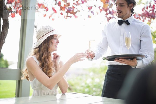 Kellnerin serviert Champagner für junge Frau im Gartenrestaurant