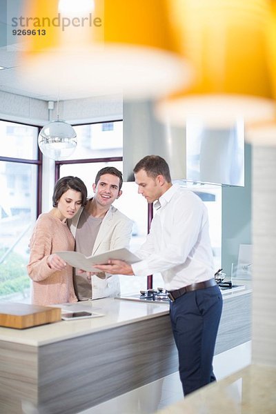 Mittleres erwachsenes Ehepaar und Verkäufer beim Betrachten der Broschüre im Küchen-Showroom