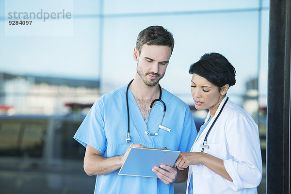 Arzt und Krankenschwester beim Lesen der Krankenakte im Freien