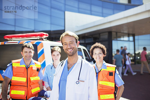 Arzt lächelt mit Sanitätern auf dem Krankenhausparkplatz