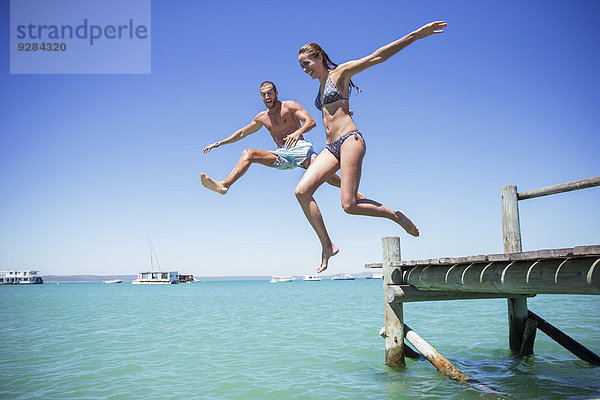 Paar springt vom Holzsteg ins Wasser