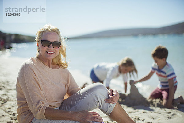 Ältere Frau am Strand sitzend mit Familie