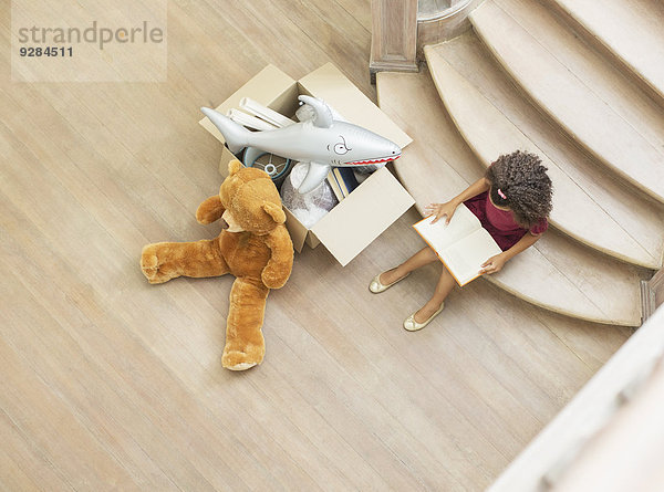 Junges Mädchen liest auf einer Treppe mit Spielzeug