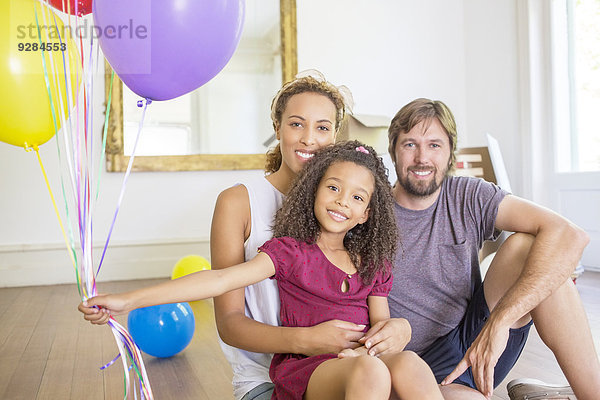 Familie sitzend im Wohnraum mit Luftballons