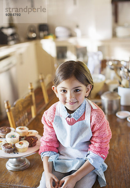 Junges Mädchen auf Küchentisch bei Muffins sitzend